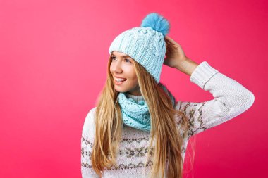 Beautiful girl standing isolated on red background, in warm blue hat and warm scarf. Concept, winter, cold, warm clothes clipart