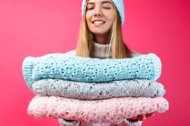 The girl in the blue warm hat, holding scarves on a red background. Winter, cold, warm clothes clipart