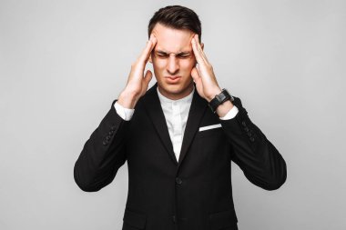 Yakışıklı genç iş adamı, Erkek klasik siyah elbiseli, gri bir arka plan karşı güçlü bir baş ağrısı hissediyor.
