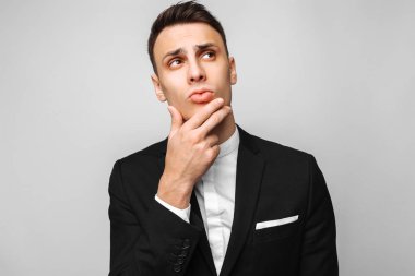 Rüya gibi genç iş adamı, klasik siyah bir takım elbise, bir erkekte düşünceli tarafında gri bir arka plan görünüyor. İş kavramı, kariyer.