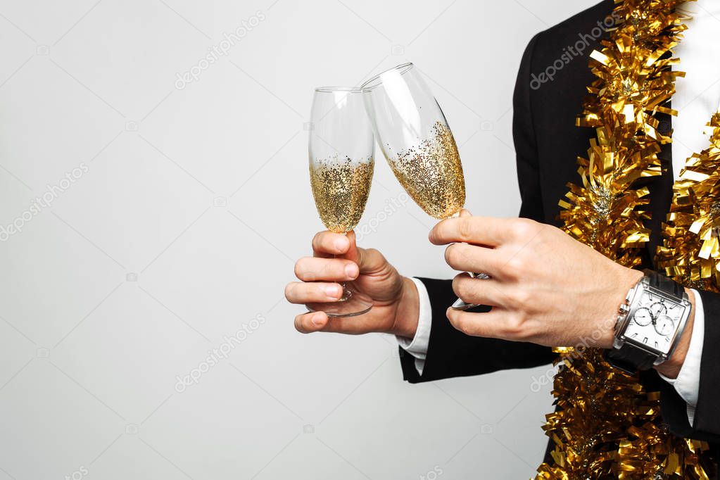 attractive man in a business suit, and with a tinsel around his neck, a man holding a glass of champagne, on a gray background. The concept of the new year.