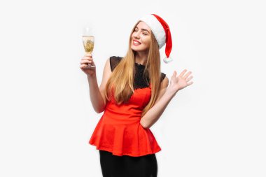 Happy young woman wearing a dress and Santa hat, celebrating the new year, in her hands, a glass of champagne, on a white background. Christmas concept. clipart