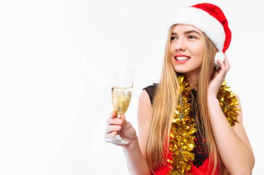 Onun elinde, bir kadeh şampanya, beyaz bir arka plan üzerinde yeni yıl kutlama bir elbise ve Noel Baba şapkası, giyen mutlu genç kadın. Noel kavramı.
