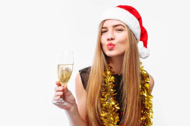 Onun elinde, bir kadeh şampanya, beyaz bir arka plan üzerinde yeni yıl kutlama bir elbise ve Noel Baba şapkası, giyen mutlu genç kadın. Noel kavramı.