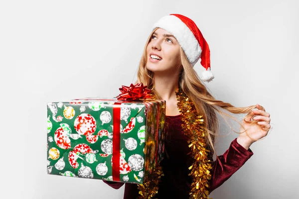 Nachdenkliches Mädchen Mit Weihnachtsmannhut Ihren Händen Weihnachtsgeschenke Auf Weißem Hintergrund — Stockfoto