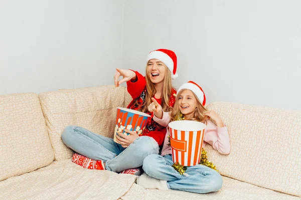 Genç bir anne ve küçük kızı Noel Baba şapkaları, giyinip, film izlemek ve evde kanepede otururken patlamış mısır yemek. Noel kavramı