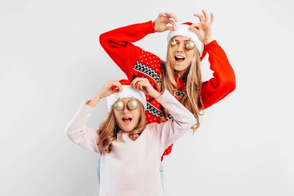 ママと娘は 新年のセーターでサンタ クロースの帽子を着ている クリスマス ボールと遊ぶことによって 新年を祝います 白い背景に ロイヤリティフリーのストック画像