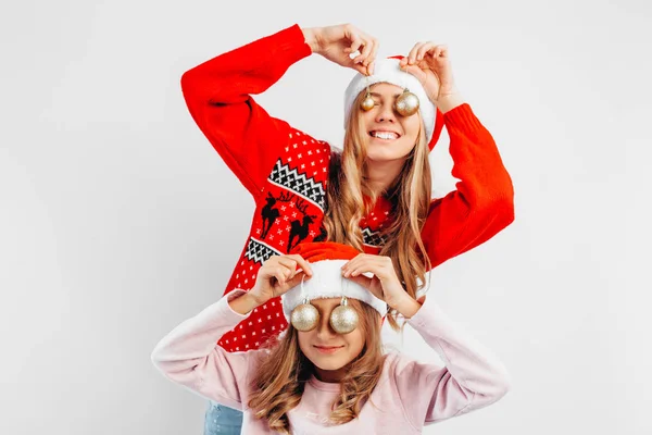 ママと娘は 新年のセーターでサンタ クロースの帽子を着ている クリスマス ボールと遊ぶことによって 新年を祝います 白い背景に ストック画像