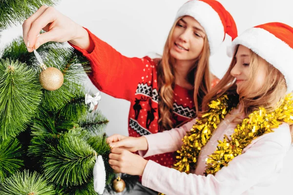 Mutter Und Tochter Schmücken Mit Weihnachtsmann Hüten Gemeinsam Den Weihnachtsbaum lizenzfreie Stockfotos