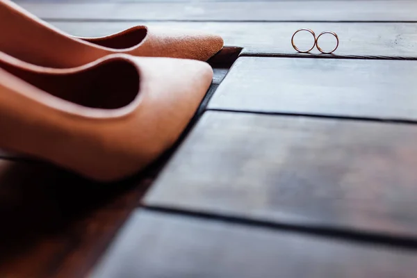 时尚优雅的经典米色的新娘鞋 两个结婚戒指躺在一个木制的背景 — 图库照片