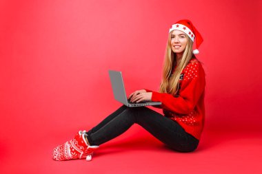 İş kız kırmızı kazak ve Santa şapka oturma laptop ile kırmızı arka plan üzerinde çalışıyor. Noel, iş kavramı,