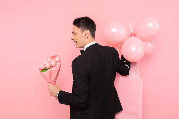 elegant man, in a suit, with a bunch of flowers, and balloons, on a pink background