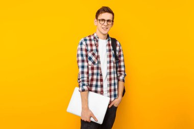 Mutlu gözlüklü, el, sarı bir arka plan üzerinde kapalı bir dizüstü bilgisayar ile bir ekose gömlekli bir öğrenci