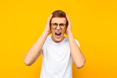 Gözlüklü, beyaz bir tişört, bir adam agresif giyinmiş tahriş olmuş adam bağırır ve sarı bir arka plan üzerinde onun kulaklarını kapatır