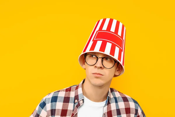 メガネで陽気な男は黄色の背景に 彼の頭にポップコーンのバケツで 映画を鑑賞する幸せ — ストック写真