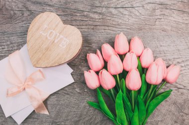 Buket pembe laleler, tahta kalp ve ahşap arka plan, üstten görünüm üzerinde beyaz zarf. Kadınlar günü