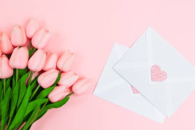 Bir buket pembe laleler ve boş beyaz mektup zarfları, pembe bir arka plan üzerinde eller. Yukarıdan görüntüleyin. Kadınlar günü
