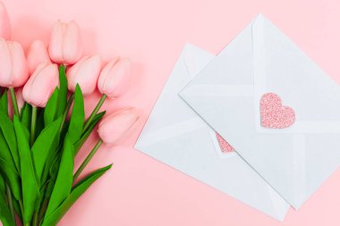 Bir buket pembe laleler ve boş beyaz mektup zarfları, pembe bir arka plan üzerinde eller. Yukarıdan görüntüleyin. Kadınlar günü