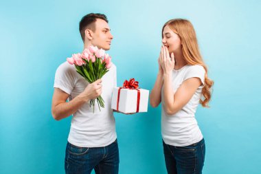 Çekici bir adam kız arkadaşı buket laleler ve mavi bir arka plan beyaz tişörtler giymiş bir hediye verir. Sevgililer günü