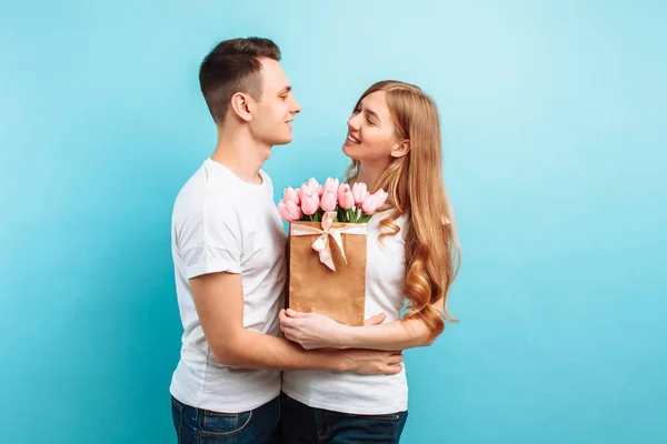 魅力的な男は 青色の背景に彼のガール フレンドのピンクのチューリップの花束を与えます バレンタインの日 — ストック写真