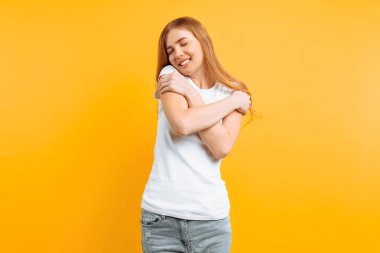 Beyaz bir T-shirt mutlu sevimli kız kendini omuz ve sarı bir arka plan üzerinde bir şey hayalleri hugs
