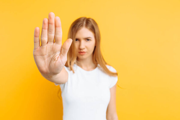 Young serious girl in a white T-shirt shows a forbidding gesture on a yellow background