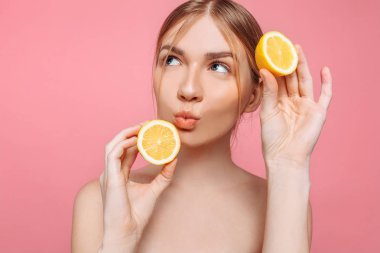 Bir neşeli kadınsı kız, doğal açık cilt, pembe bir arka plan üzerinde izole iki limon dilimleri ile kız portresi. Cilt bakım kavramı, doğal güzellik