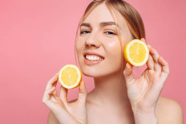 Bir neşeli kadınsı kız, doğal açık cilt, pembe bir arka plan üzerinde izole iki limon dilimleri ile kız portresi. Cilt bakım kavramı, doğal güzellik