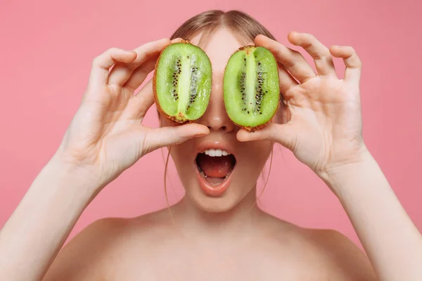 Aantrekkelijk meisje kiwi segmenten, te houden op een roze achtergrond. Natur — Stockfoto