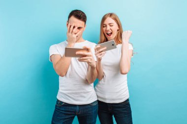 Genç çift ayakta, cep telefonlarında oyun heyecanlı, 