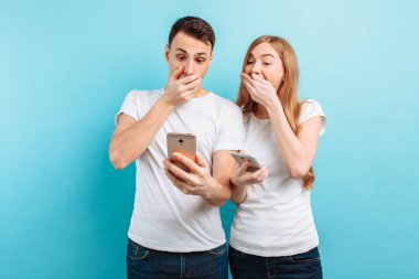 Şok insanlar, erkek ve kadın, ellerinde mavi bir arka plan üzerinde akıllı telefonlar tutarak fotoğraf