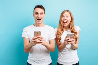 Fotoğraf heyecanlı insanlar, erkek ve kadın, sevindirici, akıllı telefonlar açık mavi renkli ellerinde tutan