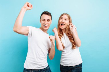 Heyecanlı bir çift, bir adam ve bir kadın kutluyor zafer yükseltilmiş, yumruk ile portresi çığlık, açık mavi arka planı üzerinde
