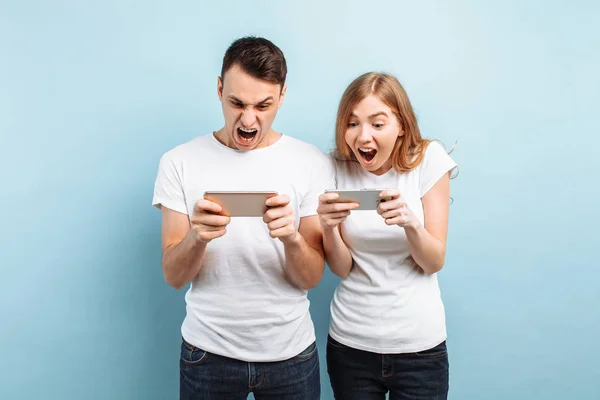 Young excited couple standing , playing games on mobile phones,