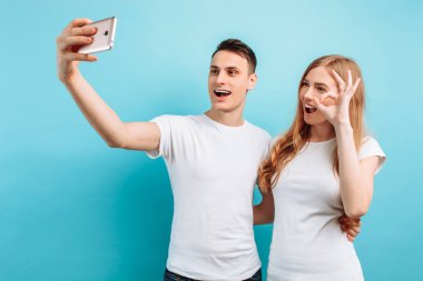 erkek ve kadın selfie bir smartphone ve yaygın olarak gülümseyen alarak mutlu bir çift, bir jest sırada gösterilen.