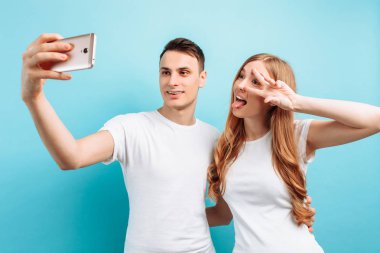 erkek ve kadın selfie bir smartphone ve yaygın olarak gülümseyen alarak mutlu bir çift, iki parmak mavi arka plan üzerinde gösterilen.