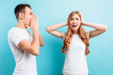 bir genç, agresif adam bir kadına bağırıyor, bir kadın mavi bir arka plan üzerinde elleriyle kulaklarını kapsar.