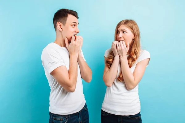 Of a young couple, frightened man and woman, holding hands near the mouth, frightened expressions, on a blue background — Stock Photo, Image