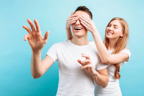 Of a loving couple, a man and a woman, dressed a woman closes the eyes of a guy, wants to make a surprise, on a blue background — Stock Photo, Image