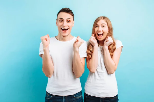 Of an emotional pair of a man and a woman screaming with surprise or delight and raising their hands against a blue background — Stock Photo, Image