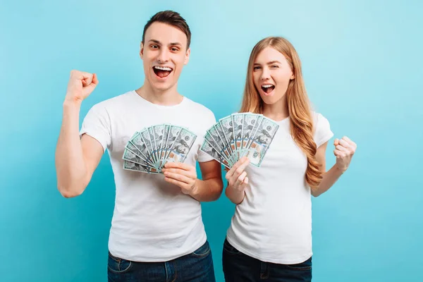 Di una giovane coppia felice, un uomo e una donna in possesso di denaro fa un gesto vincente, su uno sfondo blu . — Foto Stock