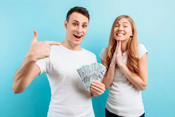 Foto di una giovane coppia felice innamorata, uomo e donna, vestita con denaro in mano, su uno sfondo blu — Foto Stock