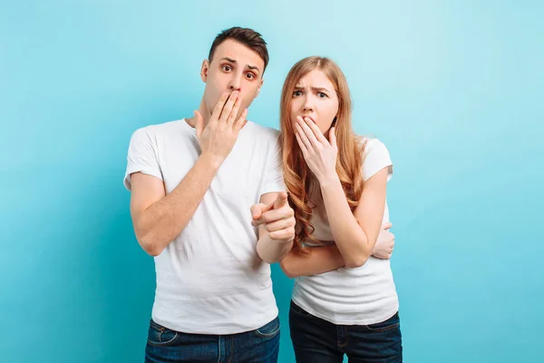 Of a young couple, frightened man and woman, holding hands near the mouth, frightened expressions, on a blue background — Stock Photo, Image