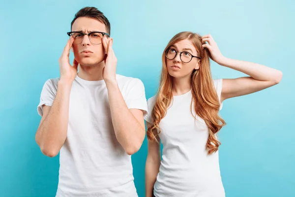 Hombre y mujer con gafas, enfocados y pensativos, sobre un fondo azul claro . — Foto de Stock