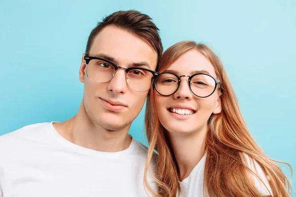 De um jovem casal feliz, vestindo óculos, homem e mulher, sorrindo, olhando para a câmera, contra um fundo azul — Fotografia de Stock