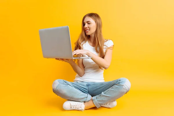 Retrato de una joven sonriente, sentada con las piernas cruzadas usando un portátil, sobre un fondo amarillo —  Fotos de Stock