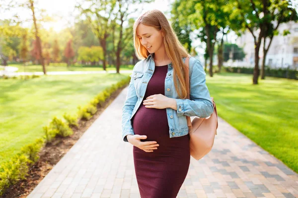 Счастливая беременная девушка обнимает свой живот во время прогулки в па — стоковое фото