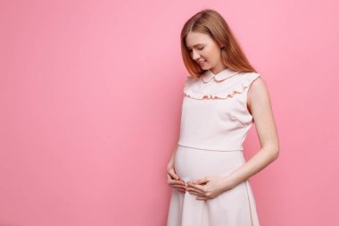 Güzel hamile kadın pembe bir arka plan üzerinde karnını okşayarak