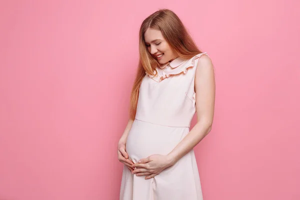 Hermosa mujer embarazada acariciando su vientre sobre un fondo rosa — Foto de Stock