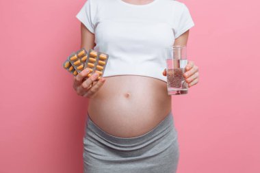 Elinde kabarcık torbaları hap tutan genç hamile bir kadının eli. Hamilelik sırasında vitamin alımı. pembe bir arka plan üzerinde